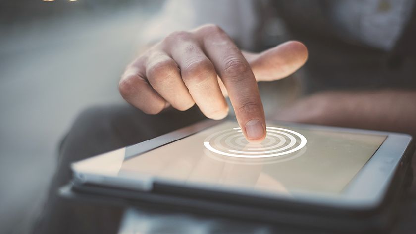 A mão de uma pessoa toca com o dedo indicador a tela de um tablet para fazer o primeiro acesso ao Banco CNH. No ponto de contato, surge um gráfico digital luminoso de círculos.