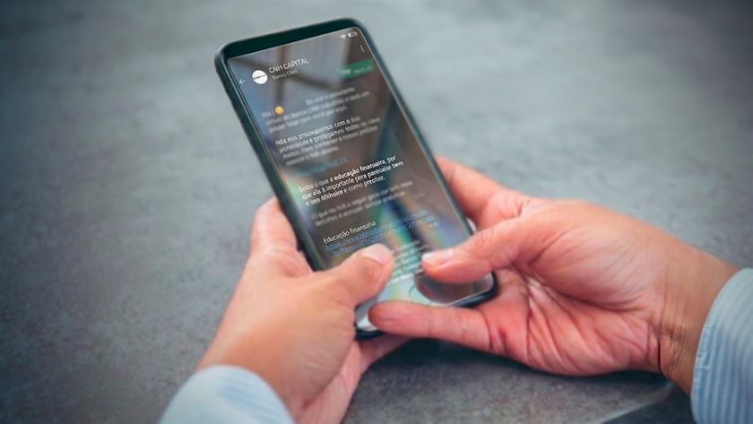 Mãos seguram um smartphone sobre uma superfície cinza, navegando no aplicativo de mensagens Whatsapp.