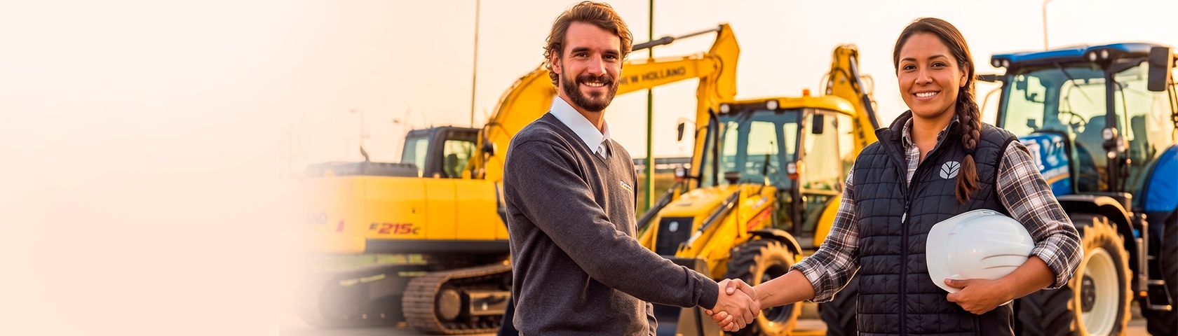 Um homem e uma mulher sorridentes apertam as mãos em frente a máquinas pesadas da New Holland amarelas e azuis.